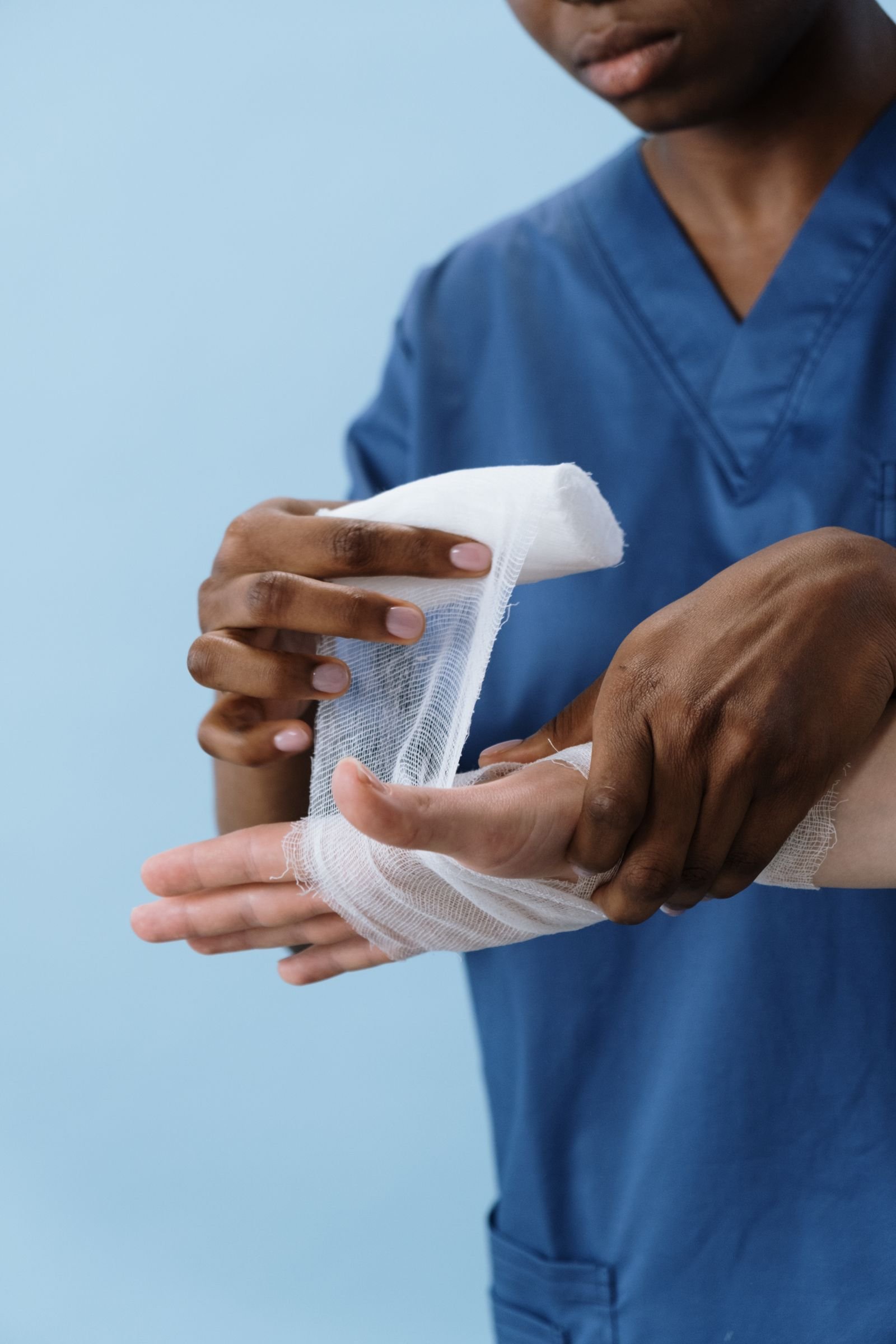 A clinician in scrubs carefully dressing a patient's hand wound